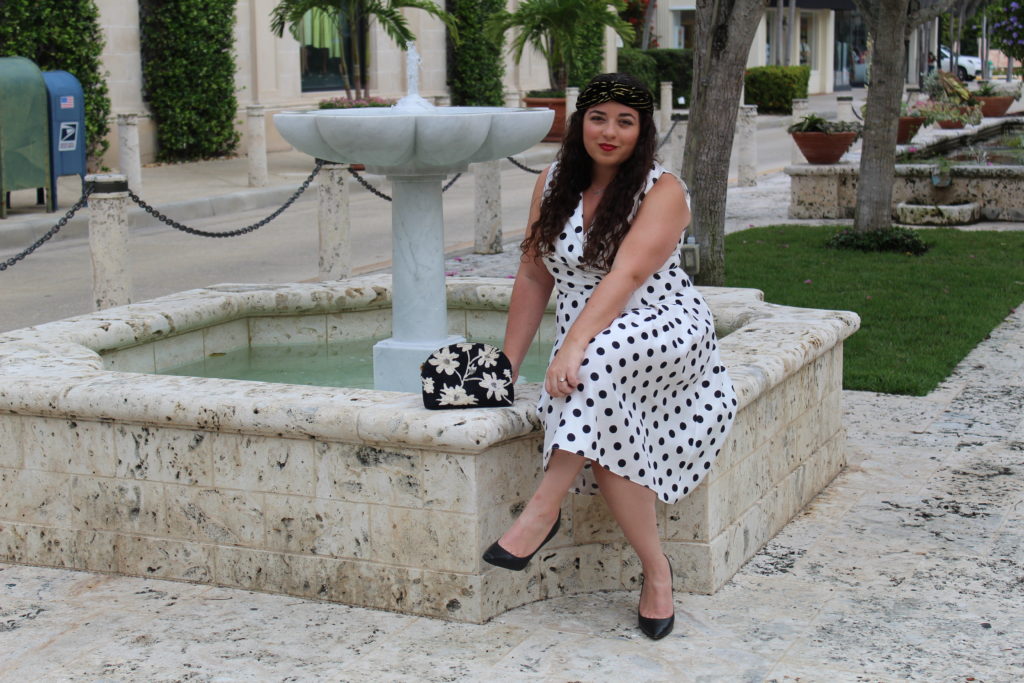 sitting at a water fountain in Palm Beach wearing a white with black polka dot dress
