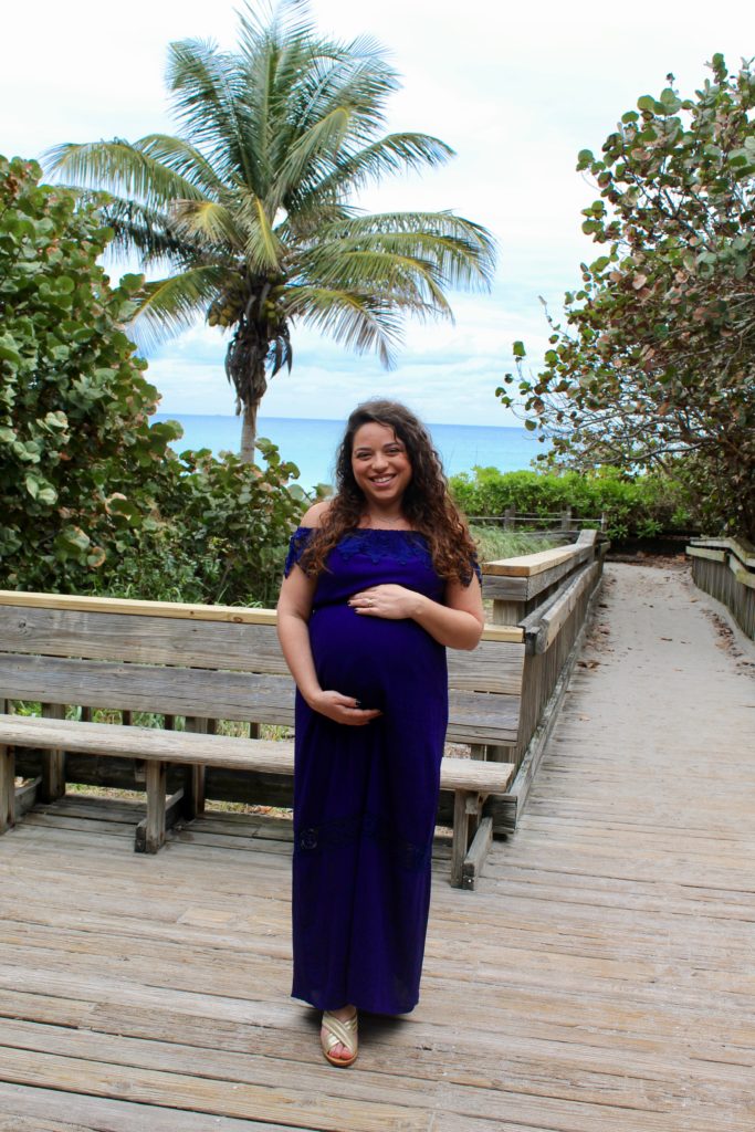 holding belly in navy blue off the shoulder dress in front of palm trees