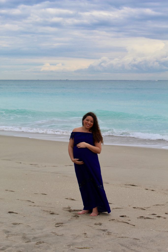 pregnant woman holding belly for maternity pictures on the beach