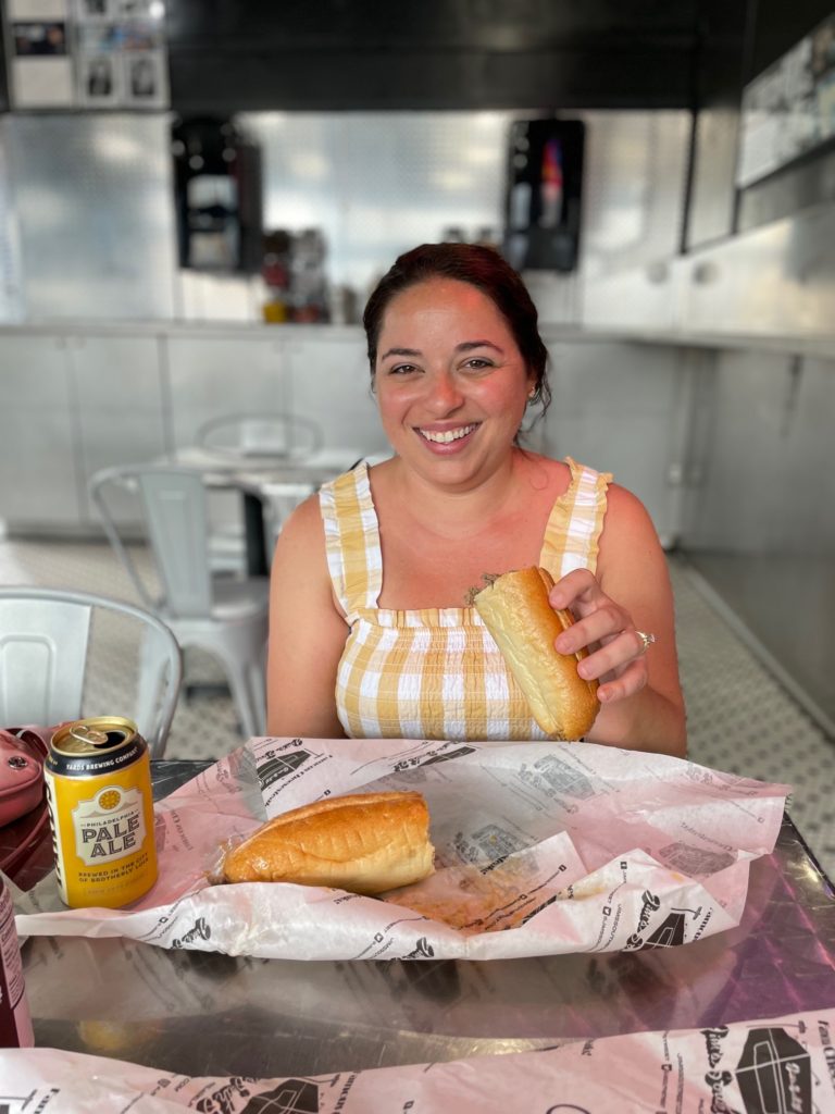 girl smiling, holding a Philly cheesesteak from Jim's South Street